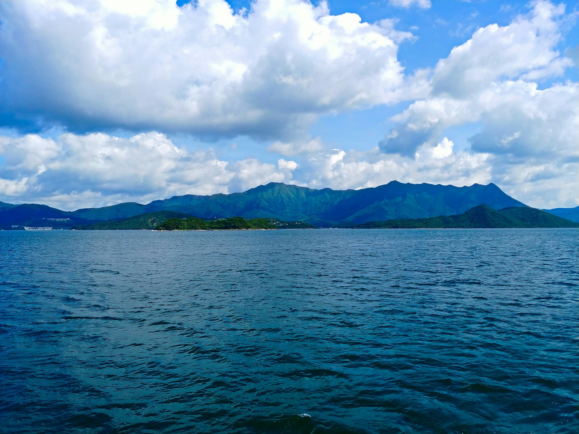 body of water near mountain under white clouds and blue sky during daytime